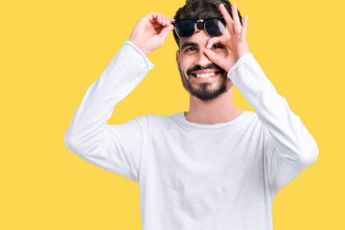 Yakışıklı delikanlı gülümseyen, parmakları ile mutlu yüz üzerinden seyir göz el ile ok jest yapıyor izole arka plan üzerinde güneş gözlüğü takıyor.
