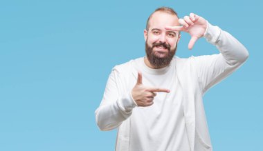 Genç beyaz hipster adam elleriyle yapım çerçeve ve parmakları ile mutlu yüz gülümseyen izole arka plan üzerinde spor kıyafetlerle. Yaratıcılık ve Fotoğrafçılık kavramı.