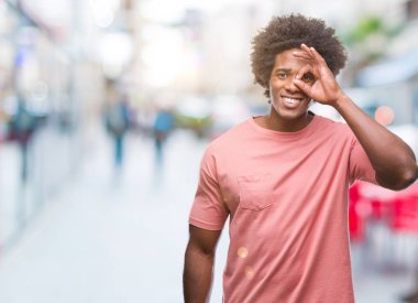 Afro Amerikalı adam gülümsüyor, parmakları ile mutlu yüz üzerinden seyir göz el ile ok jest yapıyor izole arka plan üzerinde.