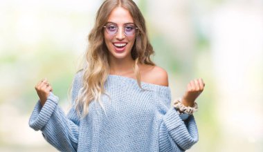 Sarışın kadın izole arka plan kutlama üzerinde güneş gözlüğü takıyor şaşırttı ve silah ile başarı için hayran güzel genç kaldırdı ve gözleri açık. Kazanan kavramı.