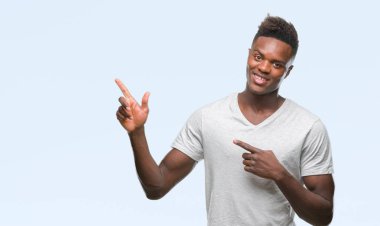 Gülümseyen ve iki elleri ve parmakları ile tarafına işaret kamera bakarak izole arka plan üzerinde genç Afro-Amerikan adam.