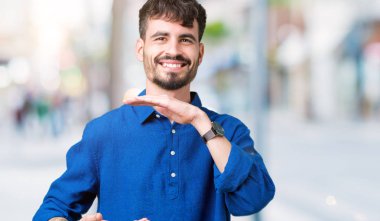 Yakışıklı delikanlı ile büyük ve büyük boy işaret, ölçü birimi sembol gösteren el eller izole arka plan üzerinde. Kameraya bakarak gülümsüyordu. Ölçüm kavramı.