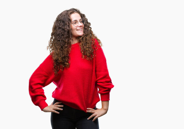 Beautiful brunette curly hair young girl wearing glasses and winter sweater over isolated background looking away to side with smile on face, natural expression. Laughing confident.