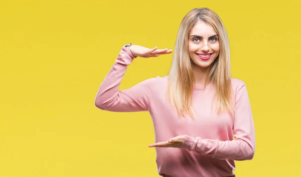 年轻美丽的金发碧眼的女人穿着粉红色的冬季毛衣在孤立的背景示意与手显示大和大尺寸的标志 测量符号 看着镜头微笑 测量概念 — 图库照片