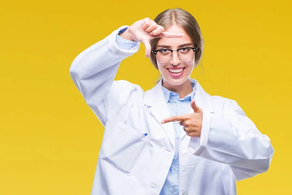 Beautiful young blonde doctor woman wearing white coat over isolated background smiling making frame with hands and fingers with happy face. Creativity and photography concept.