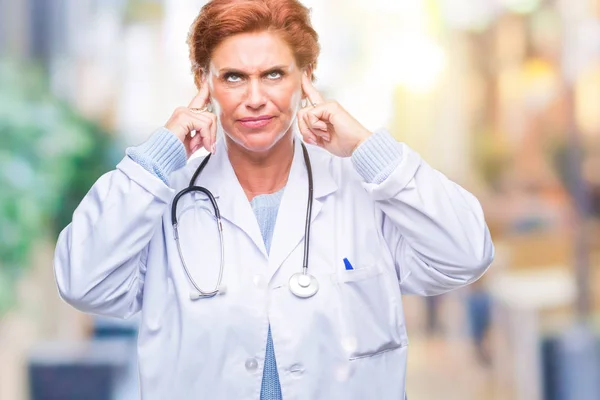 高级白种人医生妇女穿着医疗制服在孤立的背景覆盖耳朵与手指与愤怒的表达大声的音乐的噪音 聋哑人的概念 — 图库照片