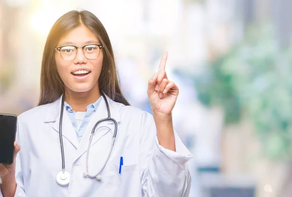 年轻的亚洲医生妇女拿着智能手机在孤立的背景惊讶的想法或问题用快乐的脸指指点点 — 图库照片
