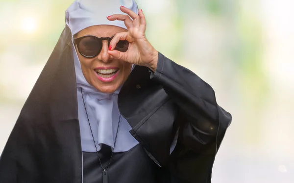 幸せそうな顔で指を通して見る目の手で のジェスチャーを行う分離の背景の上にサングラスをかけている中年シニアのカトリック修道女女 — ストック写真