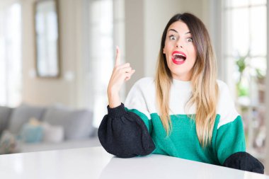 Genç güzel kadın giyiyor kış kazak evde parmak ile başarılı fikir işaret. Çıktıktan ve mutlu. Bir numara.