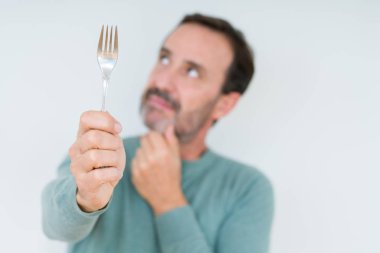 Komuta sizde holding gümüş çatal izole arka plan ciddi bir yüz düşünme hakkında soru, çok karışık bir fikir üzerinde