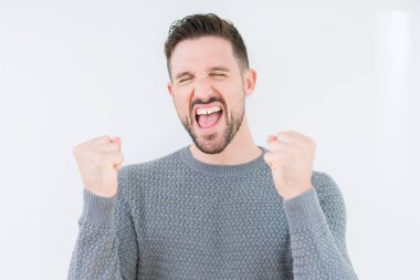 Gülümseyen ve başarı için çığlık izole arka plan çok mutlu ve heyecanlı kaldırdı, silah ile kazanan jest yapıyor üzerinde rahat kazak giyen genç yakışıklı adam. Kutlama kavramı.