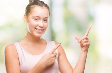 Gülümseyen ve iki elleri ve parmakları ile tarafına işaret kamera bakarak izole arka plan üzerinde beyaz genç güzel kadın.