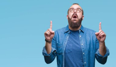 İzole arka plan üzerinde gözlüklü Genç beyaz hipster adam hayret ve yukarıya bakıp parmakları ile işaret şaşırttı ve silah kaldırdı.