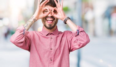 Dilini, parmaklarının arasından baktığını yapışmasını dürbün gibi ok jest yapıyor izole arka plan üzerinde pembe gömlek giymiş yakışıklı delikanlı. Deli ifade.