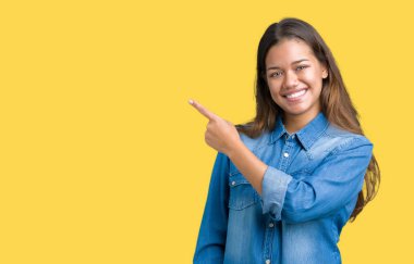 İzole arka neşeli bir gülümseme ile el ve parmak kadar yan yüzünde mutlu ve doğal ifade ile işaret yüz üzerinde mavi kot gömlek giyen genç güzel esmer kadın