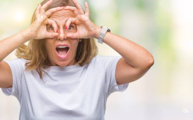 Orta yaş üst düzey İspanyol kadın dilini, parmaklarının arasından baktığını yapışmasını dürbün gibi ok jest yapıyor izole arka plan yüzünden. Deli ifade.