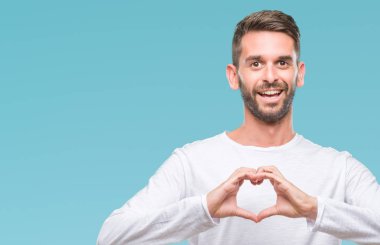 Yakışıklı delikanlı aşık kalp simgesi ve elleriyle şekil gösteren gülümseyen izole arka plan üzerinde. Romantik kavramı.