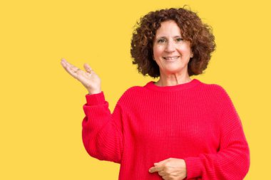 Güzel orta ager üst düzey kadın kırmızı kış kazak neşeli sunulması ve kameraya bakarak avucunun ile işaret gülümseyen izole arka plan üzerinde.