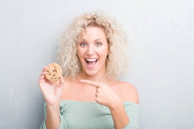 Sarışın genç kadın çikolatalı bisküvi el ve parmak ile işaret çok mutlu yemek grunge gri duvarın üzerinden