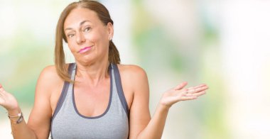 Güzel orta yaş kadın spor kıyafetlerle üzerinde arka plan clueless ve şaşkın bir ifadeyle kollar ve eller kaldırdı izole. Şüphe kavramı.