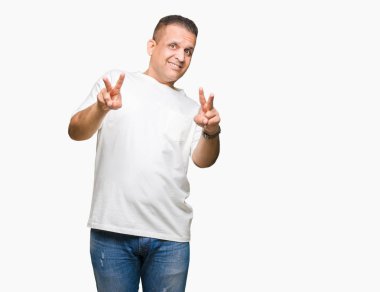 Orta yaş Arap adam wearig t-shirt zafer işareti yapıyor parmak gösterilen kamera seyir gülümseyen izole arka plan üzerinde beyaz. İki numaralı.