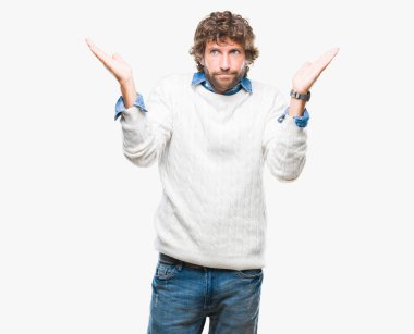 Üzerinde kış kazak giyen İspanyol yakışıklı model arka plan clueless ve şaşkın bir ifadeyle kollar ve eller kaldırdı izole. Şüphe kavramı.