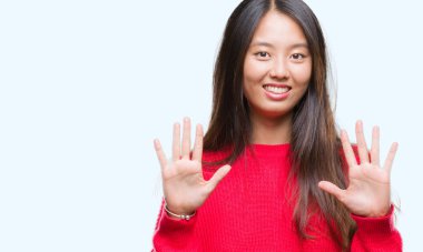 Genç Asyalı kadın giyiyor kış kazak gösterilen ve parmakları ile işaret izole arka plan üzerinde kendinden emin ve mutlu gülümseyerek süre on numara.