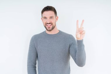 Mutlu yüz zafer işareti yaparken kameraya göz kırpıyor ile gülümseyen izole arka plan üzerinde rahat kazak giyen genç yakışıklı adam. İki numaralı.
