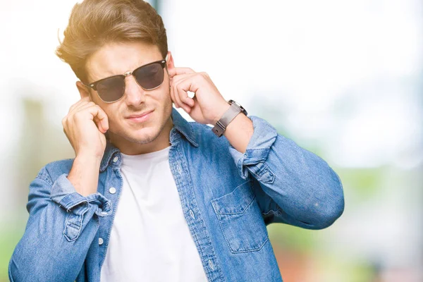 騒々しい音楽のノイズの腹式指で耳を覆う孤立の背景の上にサングラスの若いハンサムな男 聴覚障害者の概念 — ストック写真