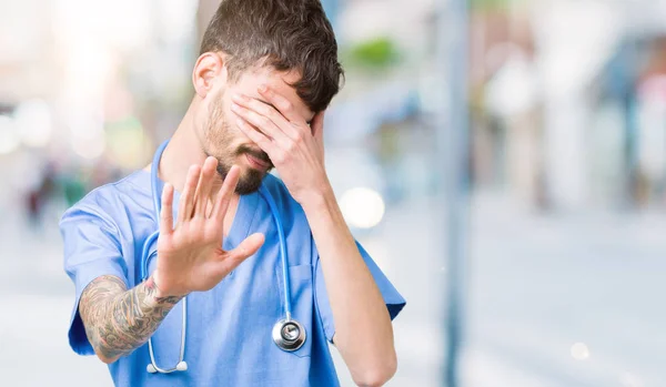 Young handsome nurse man wearing surgeon uniform over isolated background covering eyes with hands and doing stop gesture with sad and fear expression. Embarrassed and negative concept.