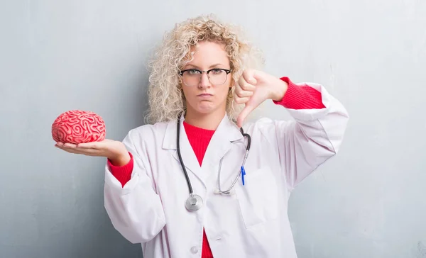 Jovem Mulher Médica Loira Sobre Grunge Cinza Parede Segurando Cérebro — Fotografia de Stock