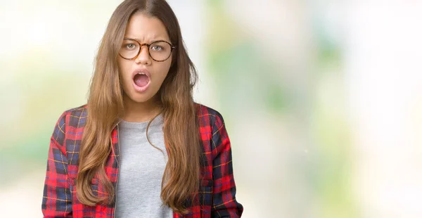 年轻美丽的黑发女人穿着夹克和眼镜在孤立的背景在震惊的脸上 看起来怀疑和讽刺 惊讶与张大的嘴 — 图库照片