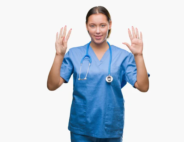 分離背景表示と指で上向きに医療制服を着ている若い白人医師女性ナンバー ナイン自信を持って 幸せな笑みを浮かべて — ストック写真