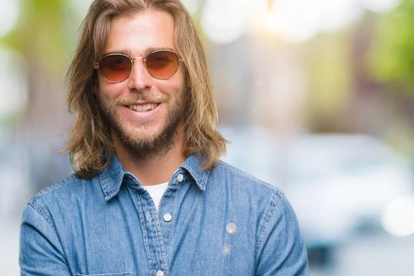 Young handsome man with long hair wearing sunglasses over isolated background happy face smiling with crossed arms looking at the camera. Positive person.
