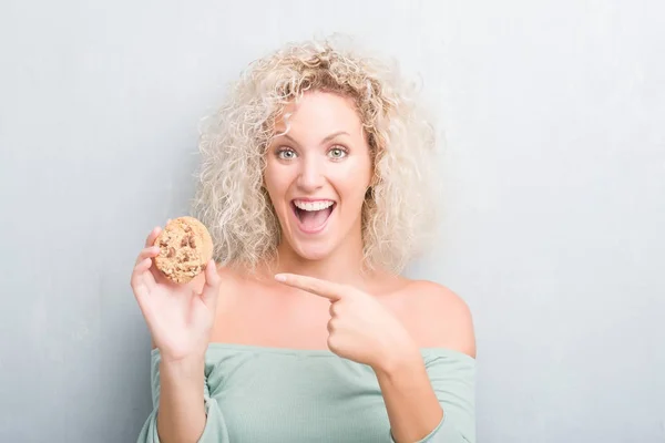 Joven Mujer Rubia Sobre Grunge Gris Pared Comiendo Chocolate Chip — Foto de Stock