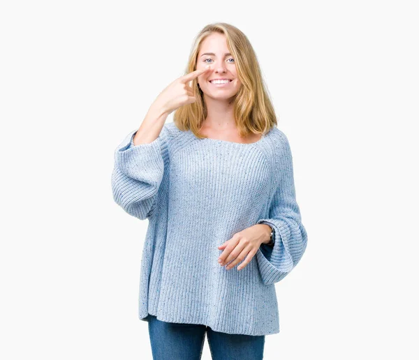 分離の上青いセーターを着ている美しい若い女性は陽気な笑みを浮かべて顔や鼻 手指でポインティングを背景します — ストック写真