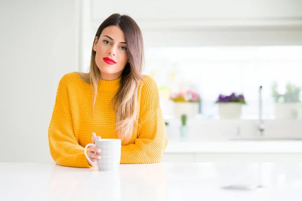 Young beautiful woman drinking a cup of coffee at home with a confident expression on smart face thinking serious