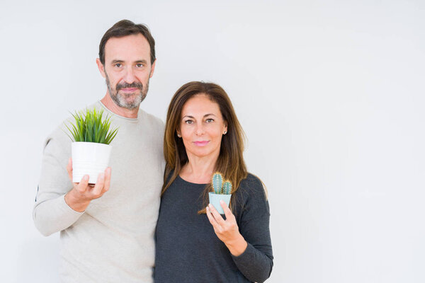 Пара средних лет держит растения на изолированном фоне с уверенным выражением на умном лице, думая серьезно
