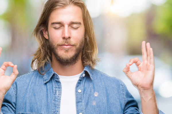 Young handsome man with long hair over isolated background relax and smiling with eyes closed doing meditation gesture with fingers. Yoga concept.