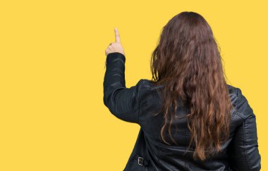 Bir moda deri ceket izole üzerinde giyen güzel artı boyutu genç kadın arka plan geriye doğru arkasında parmak eliyle işaret Posing