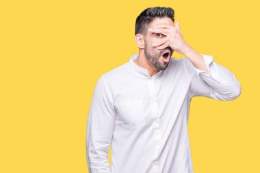 Mahcup ifadeyle parmaklarımın arasından seyir yüz ve gözler el ile kapsayan şok bakmak arka plan üzerinde genç iş adamı izole.