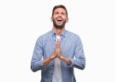 Yalvarıyor ve umut ifade yüzünde çok duygusal ve endişe ile birlikte elleriyle dua izole arka plan üzerinde beyaz t-shirt giyen genç yakışıklı adam. Bağışlanmak. Din kavramı.