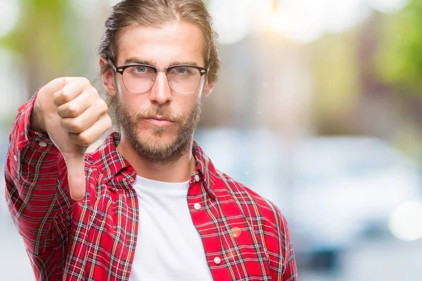 Genç yakışıklı adam uzun saçlı gözlüklü mutsuz ve kızgın ret gösterilen ve başparmak aşağı hareketi ile negatif seyir izole arka plan üzerinde. Kötü ifade.