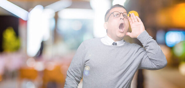 Middle age bussines arab man wearing glasses over isolated background shouting and screaming loud to side with hand on mouth. Communication concept.