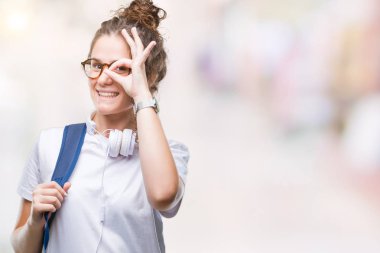 Gülümseyerek el parmakları ile mutlu yüz üzerinden seyir göz ile ok jest yapıyor izole arka plan üzerinde sırt çantası ve kulaklıklar giyen genç esmer öğrenci kız.