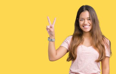 Mutlu yüz zafer işareti yaparken kameraya göz kırpıyor ile gülümseyen izole arka plan üzerinde pembe tişört giyen genç güzel esmer kadın. İki numaralı.