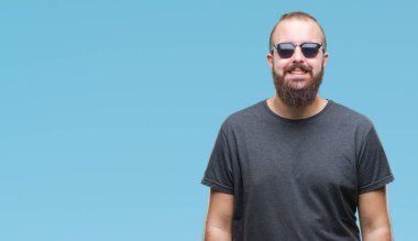 Genç beyaz hipster adam yüzünde mutlu ve güzel bir gülümseme ile izole arka plan üzerinde güneş gözlüğü takıyor. Şanslı kişi.