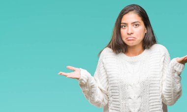 İzole arka plan clueless ve şaşkın bir ifadeyle kollar ve eller kaldırdı üzerinde kış kazak giyen genç güzel Arap kadın. Şüphe kavramı.