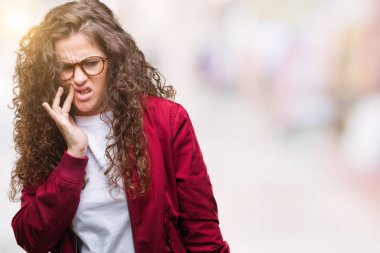 Güzel esmer kıvırcık saçlı Genç kız acı ifadesi ile el ile ağız diş ağrısı veya dişlerde dişlerle ilgili hastalık nedeniyle dokunmadan izole arka plan üzerinde ceket ve gözlük takıyor. Diş hekimi kavramı.