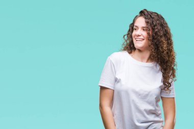Güzel esmer kıvırcık saçlı Genç kız rahat t-shirt giyen izole arka plan uzak tarafına gülümseme ile yüzünde, doğal ifade inceliyorlar. Kendine güvenen gülüyor.
